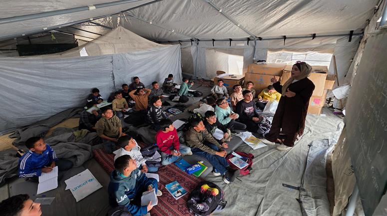 طلاب يتلقون دروساً داخل خيمة تفتقر للإمكانات الأساسية في خان يونس جنوب قطاع غزة، في ظل نقص القرطاسية والمقاعد